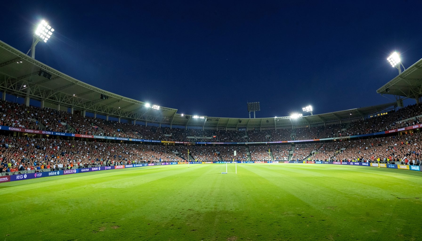 Floodlit cricket stadium at dusk with a packed crowd, green turf glowing under bright white lights against a deep navy sky