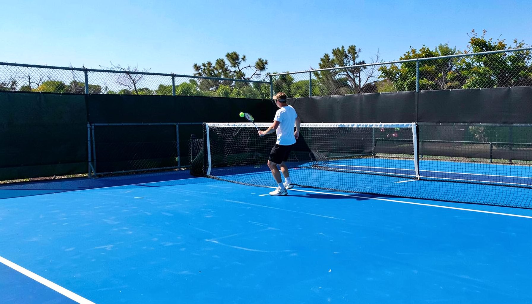 Tennis court with player serving, bright blue hard court under clear sky